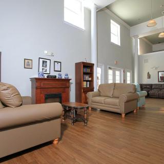 A spacious living room with sofas, a fireplace, and a bookshelf, featuring high ceilings and ample natural light from large windows.