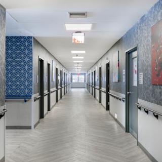A well-lit corridor in a hospital, showcasing patterned walls and multiple doors leading to patient rooms.