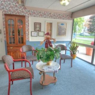 A cozy waiting room with several chairs, a table, and decorative plants near large windows.
