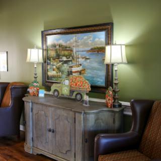 A cozy living room setup featuring a wooden console table, decorative lamps, and a tranquil landscape painting on green walls.
