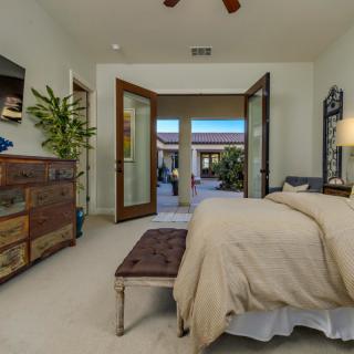 A cozy bedroom with an open door leading to a patio, featuring a bed, dresser, and decorative plant.