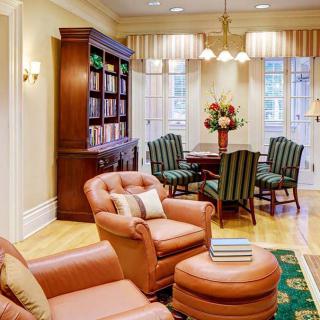 A cozy living and dining area featuring leather armchairs, a wooden bookshelf, and a dining set with striped upholstery.