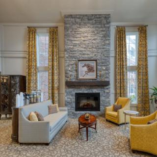A cozy living room with a stone fireplace, elegant sofa, and two yellow armchairs.