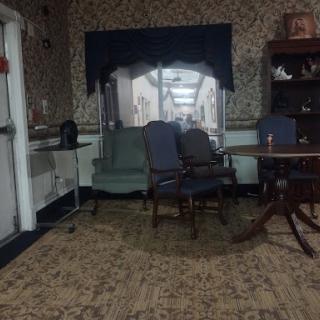 A cozy sitting area featuring a mix of chairs and a table, with warm lighting and floral wallpaper.