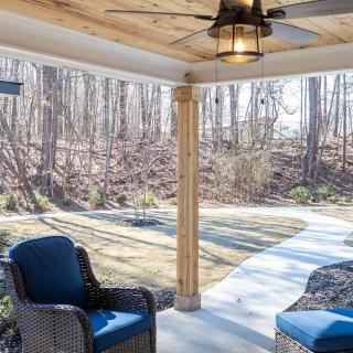 A cozy covered patio with wicker chairs, offering a scenic view of the forest.