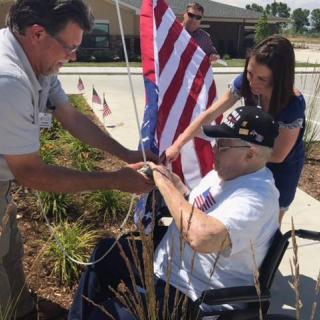 A group of people helping an elderly man in a wheelchair with an American flag outdoors.