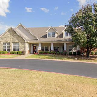 A large residential house with a porch, surrounded by a well-maintained lawn and trees under a clear blue sky.