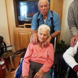 A heartwarming moment between an elderly woman in a wheelchair and a man, likely a family member, sharing quality time together indoors.
