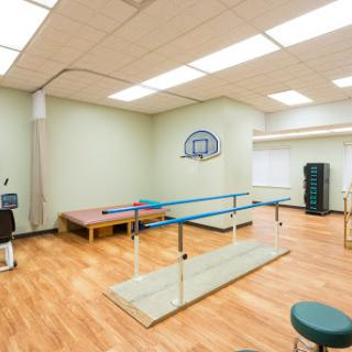 A spacious physical therapy room equipped with exercise equipment and a ballet bar for rehabilitation activities.