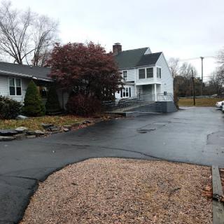 A cozy residential house with a winding driveway and surrounding trees, captured on a cloudy day.