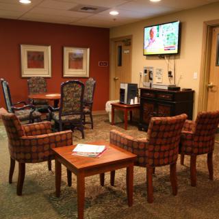 A cozy waiting room with chairs arranged around a table and a television on the wall.