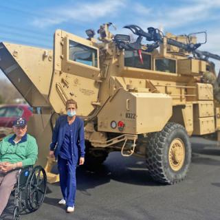 A medical professional stands next to a military vehicle while a person in a wheelchair looks on.