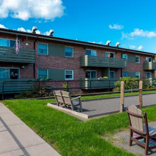 A modern residential apartment complex with green grass and outdoor seating under a clear blue sky.