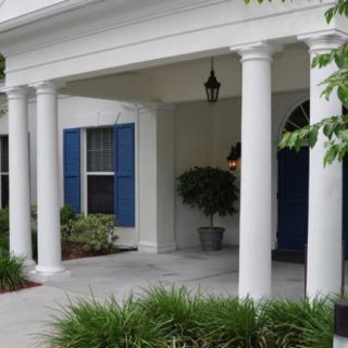 A porch with white columns, blue shutters, and potted plants.