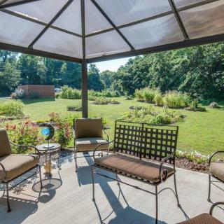 A cozy patio with comfortable seating under a gazebo, overlooking a lush green garden.