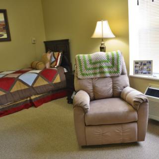 A cozy bedroom with an armchair, bed, and lamp by the window.