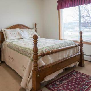 A cozy bedroom with a wooden bed and a decorative rug, featuring a large window with natural light.