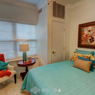 A cozy bedroom with turquoise bedding and decorative pillows, featuring a table lamp and an armchair by the window.