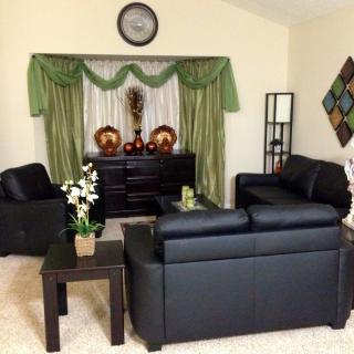 A cozy living room featuring black leather furniture, accented by green curtains and decorative pieces.
