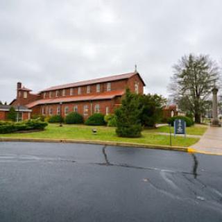 A red brick church surrounded by green landscaping under a cloudy sky.