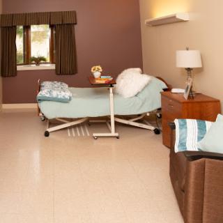 A cozy hospital room featuring a bed, bedside table, and natural light from the window.