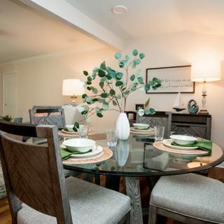 A modern dining room with a glass table, set for a meal, featuring elegant decor and artwork.
