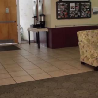 A cozy lobby area with a floral chair, floor tiles, and a coffee station against the wall.