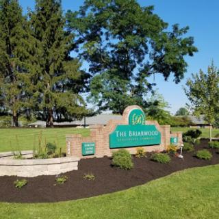 A welcoming sign for 'The Delphian' surrounded by lush greenery and clear blue skies.
