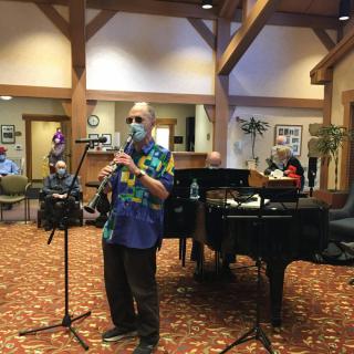 A musician performs on the clarinet in front of a grand piano, entertaining an audience indoors.