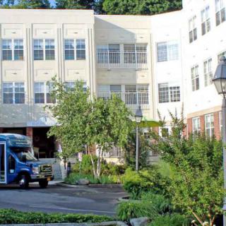 A bus parked in front of a building surrounded by greenery on a sunny day.