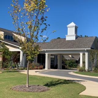 A modern building entrance with a covered driveway, lush landscaping, and a clear blue sky.