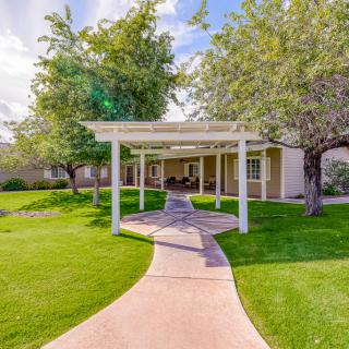 A serene garden pathway leading to a pergola, surrounded by lush greenery and trees.