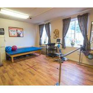 A physical therapy room equipped with parallel bars, a treatment table, and therapy balls for rehabilitation exercises.