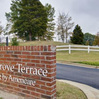A brick entrance sign for Grove Terrace near a road with trees and grass in the background.