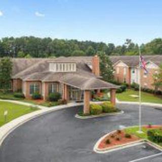A brick building with a driveway and flagpole, surrounded by trees and landscaping.