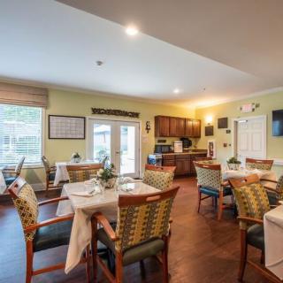 A cozy dining room with multiple tables and chairs, featuring a small kitchen area.