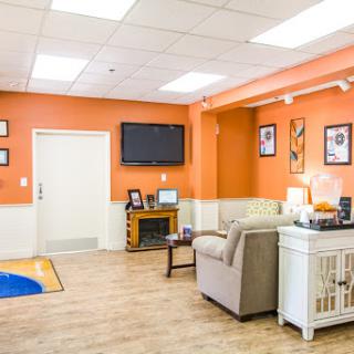 A cozy waiting room with bright orange walls and comfortable seating, featuring a television and decorative frames.