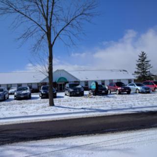A snowy scene featuring a parking lot filled with cars beside a building under a clear blue sky.