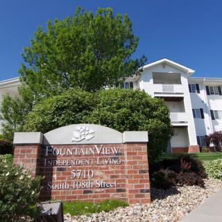 A sunny view of an apartment complex with a prominent entrance sign and surrounding greenery.