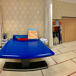A well-equipped physical therapy room featuring a blue treatment table and various exercise mats.