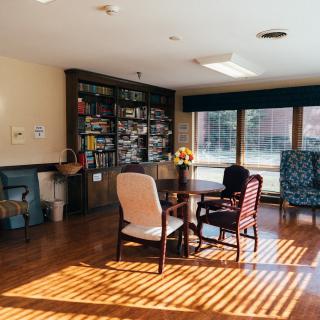 A cozy living area with comfortable seating, bookshelves, and ample sunlight streaming through large windows.