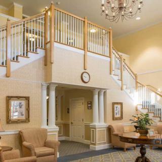 A bright and elegantly decorated lobby featuring a staircase, chandelier, and comfortable seating.