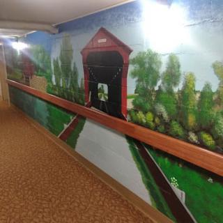 A hallway mural depicting a scenic landscape with a covered bridge.