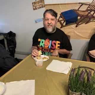 A man enjoys a meal at a dining table, wearing a colorful shirt and smiling.