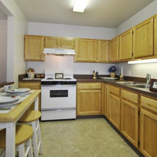 A cozy kitchen with wooden cabinets, featuring a stove, sink, and bar seating.