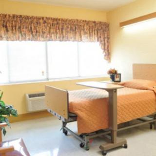 A clean and well-lit hospital room with a single bed and bedside table.