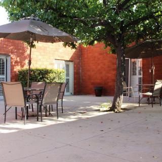A sunny patio with outdoor furniture and umbrellas next to a brick wall.