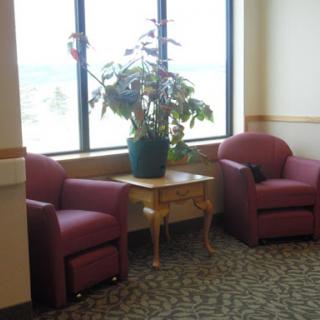 A cozy waiting area featuring two red chairs, a small table, and an indoor plant by the window.
