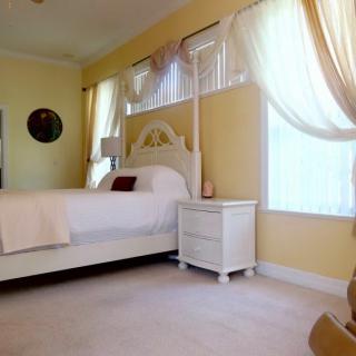 A cozy bedroom interior featuring a white bed and nightstand with light yellow walls and sheer curtains.