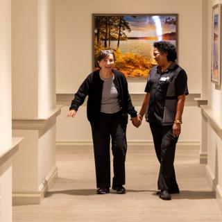 Two people walking and holding hands in a hallway, engaged in conversation.